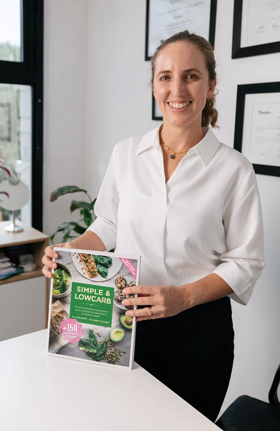 Dra. Ana Garat sosteniendo un ejemplar de su libro Simple & Lowcarb en su consultorio